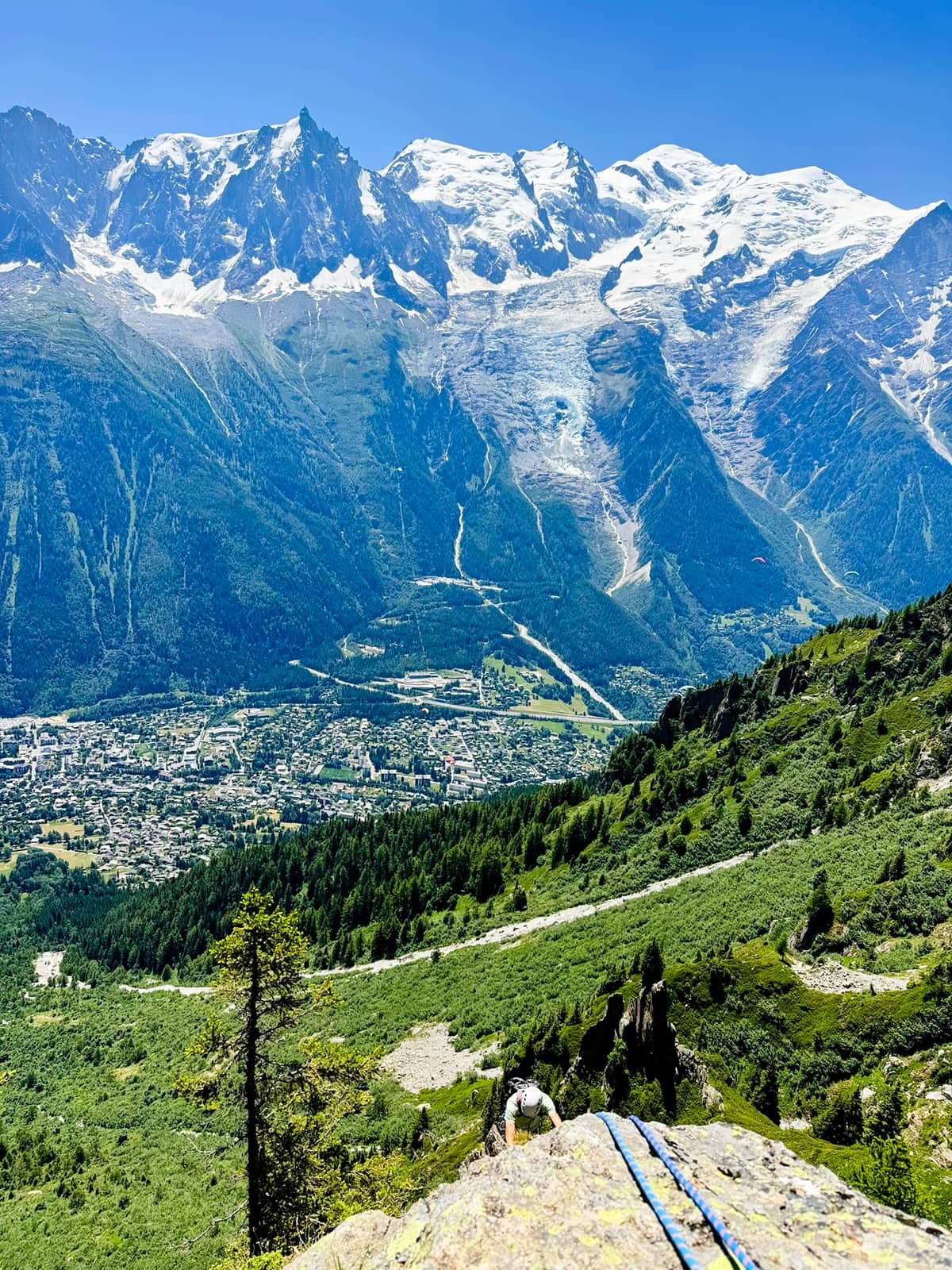 Mont Blanc and the Bossons Glacier above Chamonix, seen from high on a climbing route, with a climber coming up the rock in the foreground.